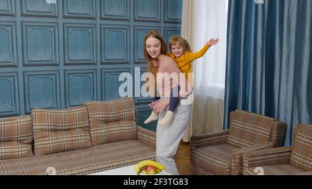 Felice famiglia madre e bambino figlia ragazzina danzare, giocare piggyback, correre, cavalcare a casa Foto Stock