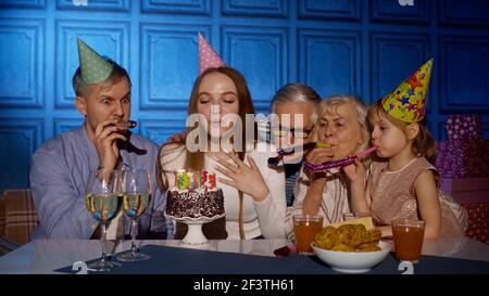 Felice donna di compleanno che soffia candele su torta facendo desiderio, divertendosi, festeggiando festa con la famiglia Foto Stock