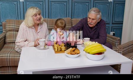 Nonni anziani e nipote che trascorrono il tempo a casa insieme, seduti, giocando a scacchi Foto Stock