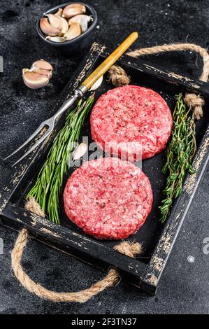 Polpettine di carne cruda per hamburger di carne macinata ed erbe su tavola di legno. Sfondo nero. Vista dall'alto Foto Stock