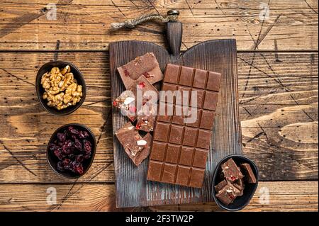 Barretta di cioccolato fondente con nocciole, arachidi, mirtilli rossi e lamponi secchi congelati su tavola di legno. Sfondo di legno. Vista dall'alto Foto Stock