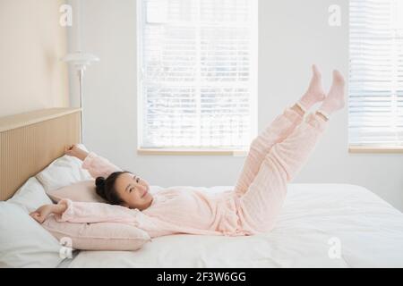 Sorridente donna asiatica felice in pigiama svegliarsi e stretching a letto Foto Stock