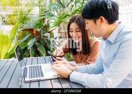 Uomo e donna asiatici che tengono la carta di credito per il pagamento su smartphone per lo shopping online seduto in un moderno cafe con computer portatile Foto Stock