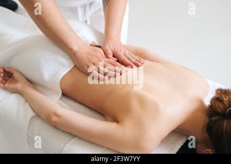 Vista dall'alto del massaggiatore maschile che massaggia la parte posteriore di una giovane donna irriconoscibile sdraiata sul tavolo da massaggio. Foto Stock