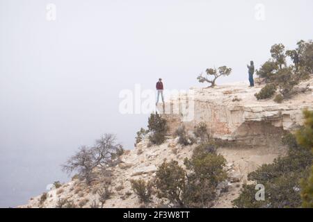 La persona si erge pericolosamente sulla scogliera a bordo del Grand Canyon nella neve invernale mentre ha la loro foto scattata. Foto Stock