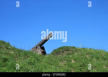 Vecchio cannone dipinto in nero installare su base di legno su verde erba pendio collina sullo sfondo di blu nuvoloso cielo in bella giornata estiva Foto Stock