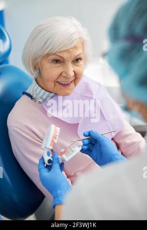 Pensionato interessato che guarda il dentista con modello dentale Foto Stock