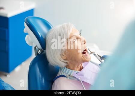 Dentista che estrae un dente di pensionato con un forcipe Foto Stock