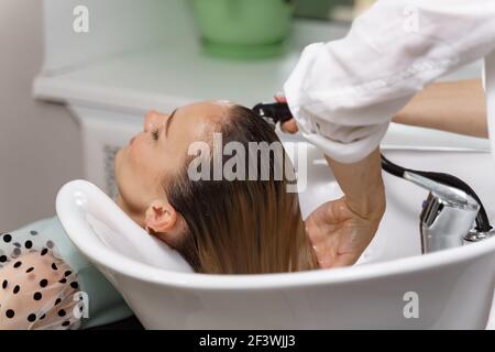 il parrucchiere lava i capelli di una giovane donna prima di un taglio Foto Stock