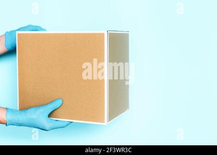 Mano in guanto medico dà scatola di mestiere su sfondo blu. Concetto di shopping online senza contatto. Banner, spazio per la copia. Trasporto di consegna veloce e gratuito Foto Stock