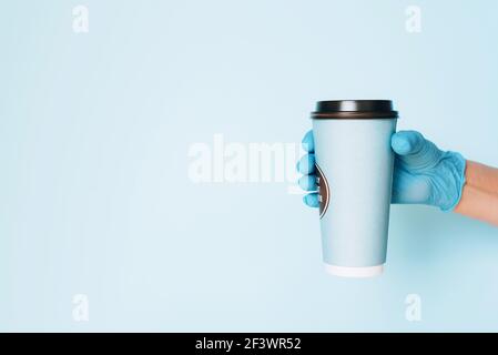 Guanti medici da portare con sé una tazza di caffè da asporto su sfondo blu. Banner con spazio per la copia. Servizio di consegna senza contatto durante Foto Stock