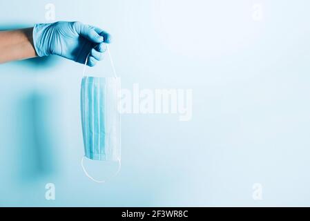 Mano con guanti medici blu che tengono maschera medica sullo sfondo. Banner con spazio per la copia. Attrezzature di protezione sanitaria durante la quarantena Foto Stock