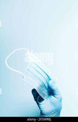 Mano con guanti medici blu che tengono maschera medica sullo sfondo. Banner con spazio per la copia. Attrezzature di protezione sanitaria durante la quarantena Foto Stock