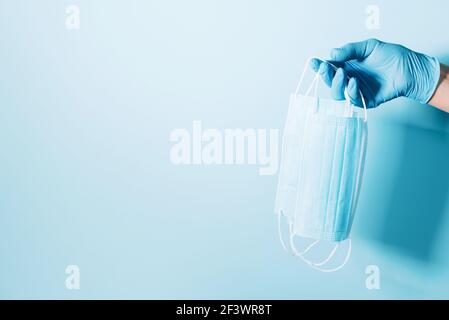 Mano con guanti medici blu che tengono maschera medica sullo sfondo. Banner con spazio per la copia. Attrezzature di protezione sanitaria durante la quarantena Foto Stock