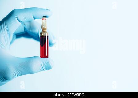 Medicina, iniezioni, concetto di vaccinazione. Mani in guanti medici che tengono la fiala con vitamina B su sfondo blu. Spazio di copia. Protezione della salute Foto Stock