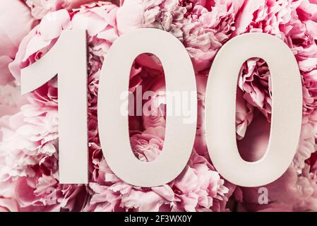 Fiori di Peony, cifra cento. Biglietto d'auguri per compleanno con iscrizione 100. Concetto di anniversario. Vista dall'alto. Numero bianco su sfondo floreale Foto Stock