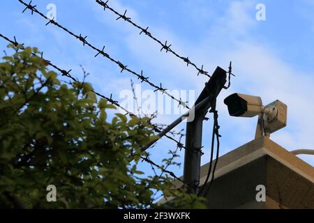 Primo piano della telecamera di sicurezza installata sul tetto accanto al barbato filo su sfondo blu Foto Stock