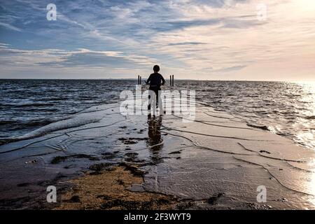 Ares (Francia sud-occidentale): Atmosfera serale al crepuscolo e tramonto sulla Baia di Arcachon in autunno. Bambino sulla sua bicicletta, i suoi piedi in acqua, di fronte t Foto Stock