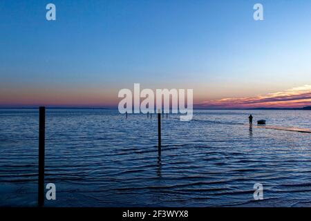 Ares (Francia sud-occidentale): Tramonto sulla baia di Arcachon in autunno. Uomo, di fronte al mare, in piedi da solo sul molo coperto da alta marea e legno Foto Stock