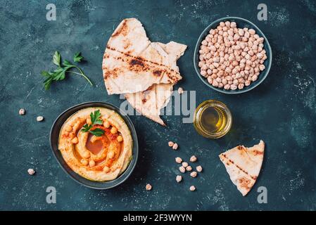 Hummus di ceci, olio d'oliva, ceci crudi, paprika affumicata, pita su fondo scuro. Cucina mediorientale, ebraica o arabica. Vista dall'alto. Copia Foto Stock