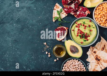 Hummus verde fatto in casa con avocado, prezzemolo, olio d'oliva, pita, ceci crudi, melograno su sfondo scuro. Cucina mediorientale, ebraica, arabica Foto Stock