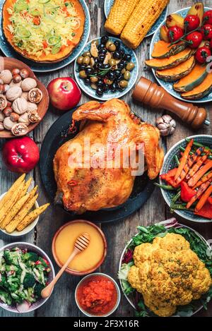 Natale o Ringraziamento pollo arrosto intero, riso, zucca, mais, miele, noci, insalate di verdure su sfondo di legno. Vista dall'alto, spazio di copia Foto Stock