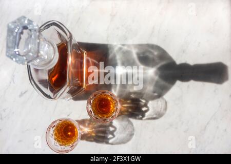 Un decanter whisky e due bicchieri su uno sfondo in marmo grigio e bianco con una moderna vista dall'alto verso il basso e una messa a fuoco intenzionale sulle ombre. Foto Stock