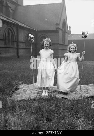 1958, storica, primaverile e due giovani ragazze in costume e tenendo bastoni di fiori in piedi su un tappeto nel terreno di una chiesa per la loro foto, prima di partecipare alla sfilata e festival del giorno di maggio, Leeds, Inghilterra, Regno Unito. Foto Stock