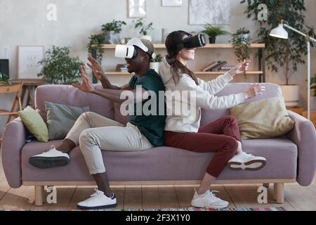 Un paio di giocatori entusiasti in occhiali vr seduti sul divano e giocare a videogame in realtà virtuale nella stanza Foto Stock