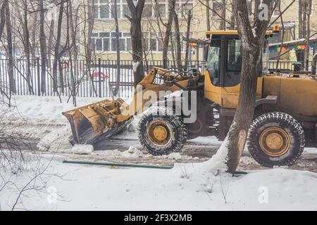 il trattore elimina la neve dalla strada nel cortile di un edificio residenziale Foto Stock