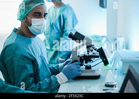 Scienziato medico in tuta nocciola che lavora con microscopio e computer portatile Computer all'interno dell'ospedale di laboratorio - Focus principale sulla mano Foto Stock