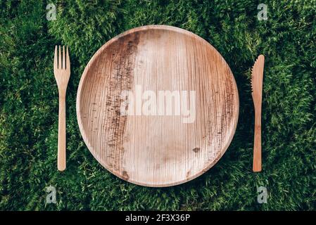 Stoviglie monouso in legno di materiali naturali, cucchiaio di legno, forchetta su fondo di muschio verde. Stile di vita sostenibile ed ecologico. Picnic senza sprechi Foto Stock