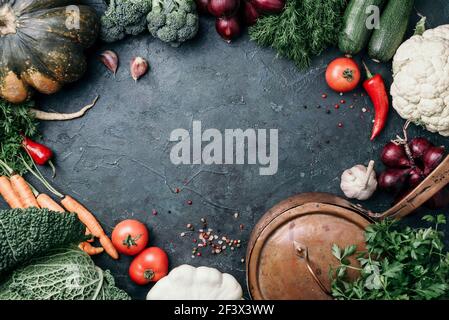 Pentola di rame, erbe, cipolla viola, zucca, pomodoro, broccoli, pepe, cavolo, carota, prezzemolo, calafiore, zucchine su sfondo scuro. Vista dall'alto. Copia Foto Stock