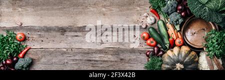 Pentola di rame, erbe, cipolla viola, zucca, pomodoro, broccoli, pepe, cavolo, carota, prezzemolo, calafiore, zucchine su fondo ligneo. Vista dall'alto. Copia Foto Stock
