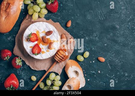 Formaggio camembert francese servito su uva, miele, mandorla, fragole, baguette su sfondo scuro. Vista dall'alto. Spazio di copia. Serata romantica Foto Stock