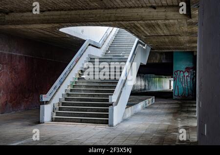 Metropolitana urbana vuota e grugnosa con scala vuota danneggiata, soffitto in cemento, piastrelle marroni usurate sul pavimento e mosaico verde sulla parete Foto Stock