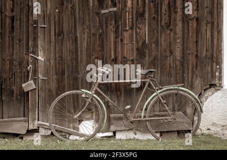 Vecchia bici vintage su erba verde appoggiata alla vecchia porta del fienile in legno, foto con effetto filtro vintage retrò Foto Stock