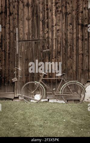 Vecchia bici vintage su erba verde appoggiata alla vecchia porta del fienile in legno, foto con effetto filtro vintage retrò Foto Stock