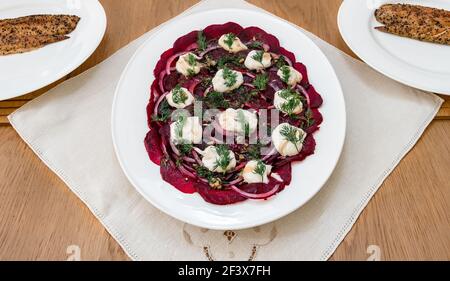 Insalata di barbabietole servita su piatto bianco con cipolle rosse, dilll e yogurt con sgombro affumicato al peperone sui piatti della cena Foto Stock