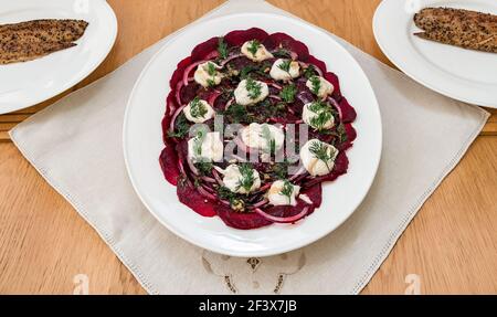 Insalata di barbabietole servita su piatto bianco con cipolle rosse, dilll e yogurt con sgombro affumicato al peperone sui piatti della cena Foto Stock