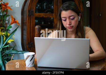 Giovane donna latina che usa il computer portatile e ascolta la musica a casa mentre beve il caffè. Concetto di home Office Foto Stock