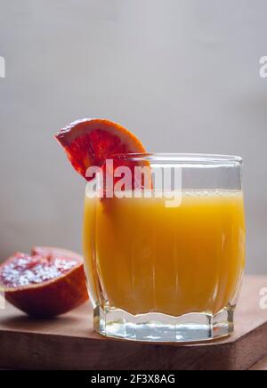 Un bicchiere di succo fresco di arance e un pezzo di arancia su un tagliere. Succo d'arancia fresco con arance a fette. Foto Stock