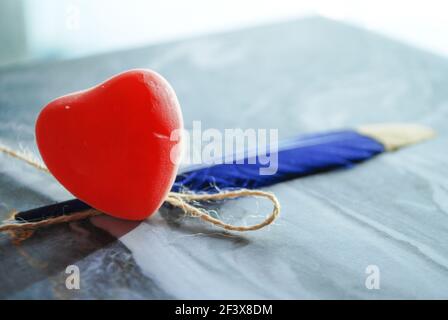 cuore di gelatina rossa con piuma blu isolato su marmo ondulato carta, sfondo sfocato della luce del giorno, sfondo romantico, spazio per qoutes e testo Foto Stock