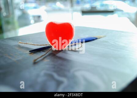 cuore di gelatina rossa con piuma blu isolato su marmo ondulato carta, sfondo sfocato della luce del giorno, sfondo romantico, spazio per qoutes e testo Foto Stock