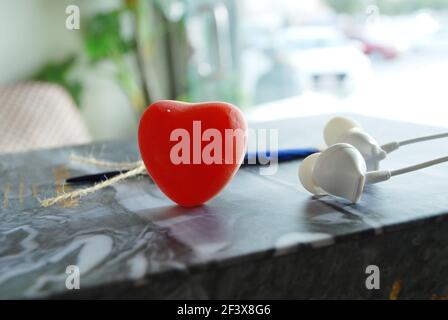 cuore di gelatina rossa con piuma blu e auricolari isolati carta ondulata in marmo, sfondo sfocato della luce del giorno, sfondo romantico, spazio per qoutes e testo Foto Stock