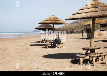 Perranporth, Cornovaglia, 18 marzo 2021, UNA signora si siede ad un tavolo tropicale durante il blocco in Perranporth, Cornovaglia in un giorno di sole. Credit: Keith Larby/Alamy Live News Foto Stock