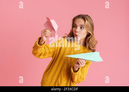 Divertente bella ragazza bionda sorridente e gettando aerei di carta isolati su sfondo rosa Foto Stock