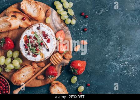 Formaggio camembert al forno con miele, rucola, mirtillo, pane tostato, uva, fragole, mandorle su fondo scuro. Vista dall'alto. Spazio di copia Foto Stock