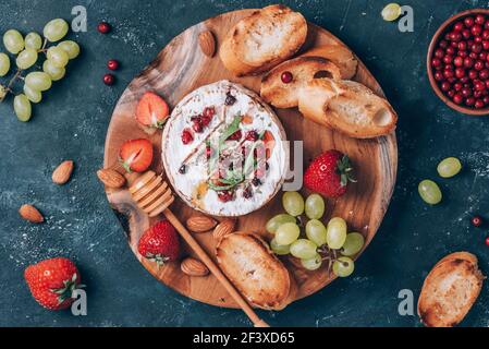 Formaggio camembert al forno con miele, rucola, mirtillo, pane tostato, uva, fragole, mandorle su fondo scuro. Vista dall'alto. Spazio di copia Foto Stock