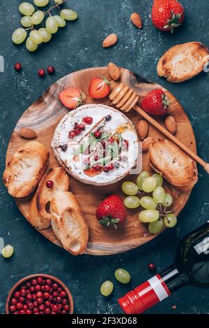 Serata romantica. San Valentino, concetto d'amore. Formaggio camembert al forno, miele, rucola, mirtillo, vino, pane tostato, uva, fragole, mandorla Foto Stock